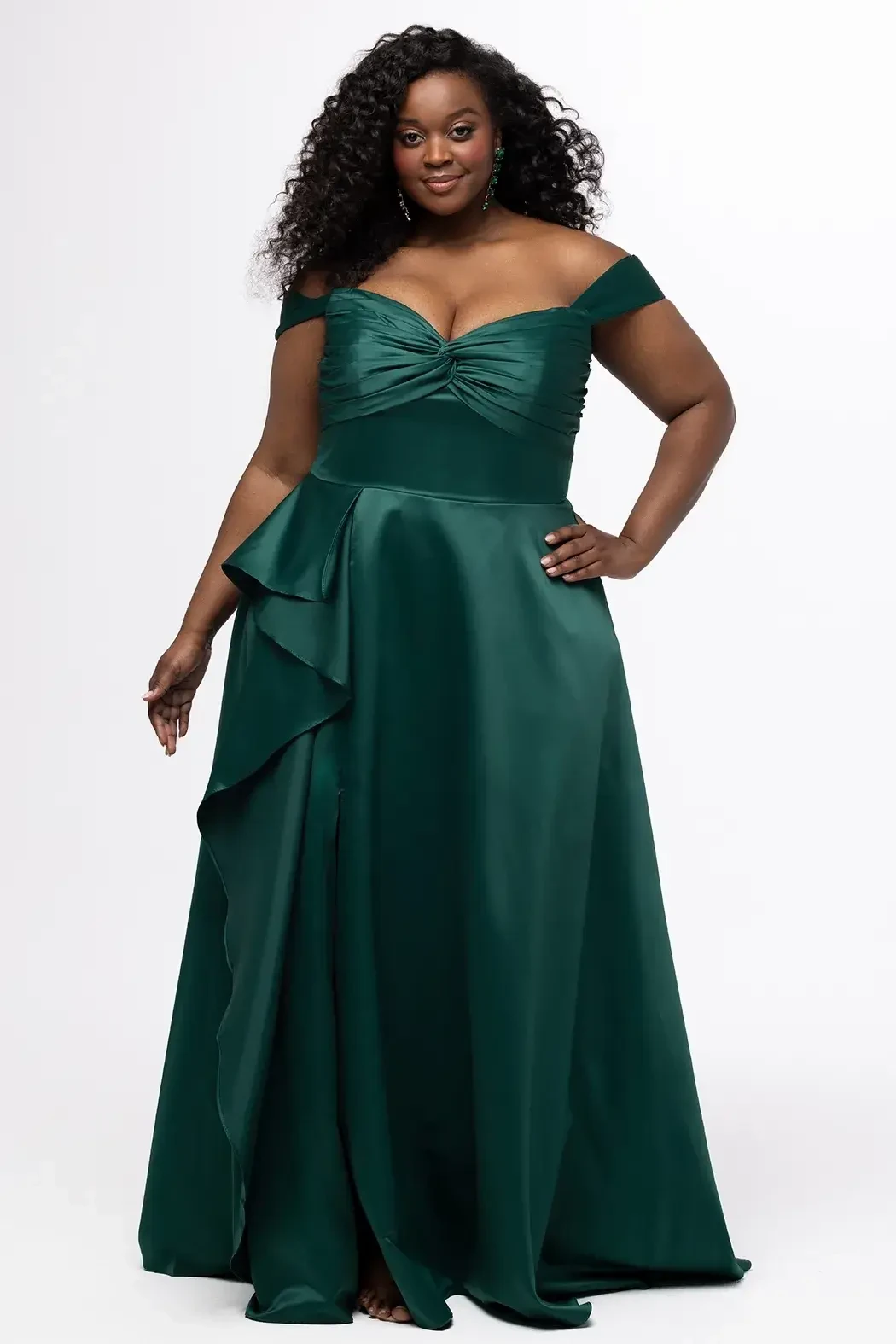 A woman wearing an off-shoulder, emerald green formal gown with a ruffled detail.
